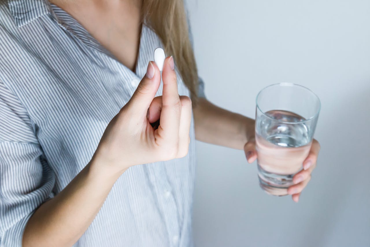 Person about to take a pill, with a glass of water in hand.