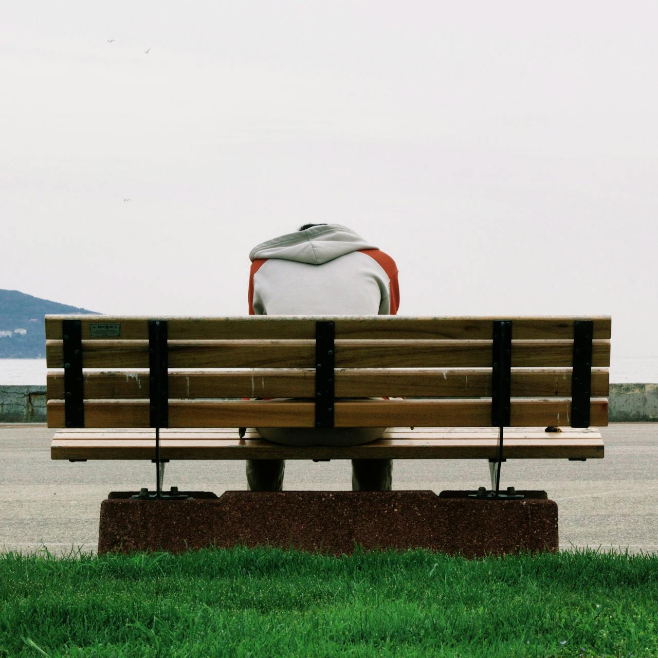 Person sitting alone on a bench, with their head drawn downward.